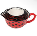 A set of nested measuring cups with a red and black ladybug-inspired design, featuring black polka dots on a red exterior, black scalloped rims, and a white interior with black printed cup measurements.